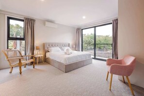 A bedroom with a large bed, a wooden chair, a small table, and a pink chair.