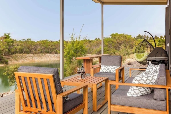 A wooden deck with outdoor furniture, including chairs and a sofa, overlooking a body of water and greenery.