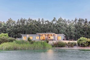 Una casa moderna junto a un lago, con un amplio balcón y zona de estar al aire libre.