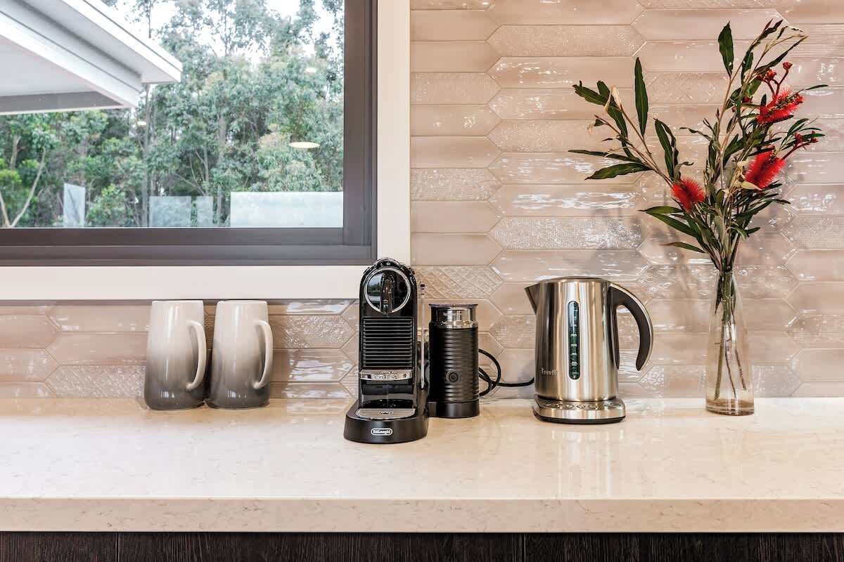 Un plan de travail de cuisine avec une machine à café, une bouilloire et un vase rempli de fleurs.