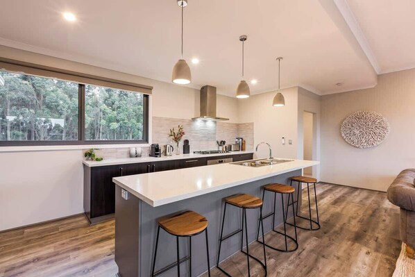 A modern kitchen with a large island, bar stools, pendant lighting, and a view of the outdoors.
