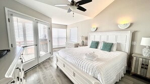 A bedroom with a large bed, a ceiling fan, and a view of the outside through the window.