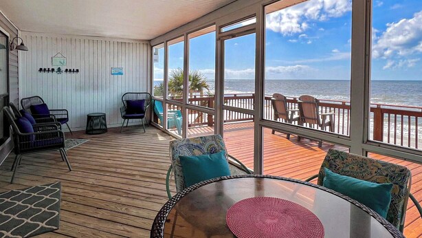 A covered deck with a view of the ocean, furnished with chairs and a table.