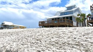 A beach house with a wooden deck and a large window overlooking the ocean.