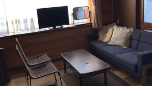 Ein Wohnzimmer mit einer Couch, einem Fernseher, einem kleinen Tisch und einem Sessel.