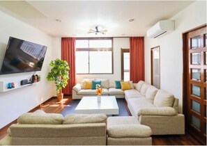 A living room with a flat-screen TV, a sofa set, a coffee table, and a potted plant.