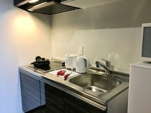 A modern kitchen with a stainless steel sink, a kettle, a toaster, and a cutting board with scissors.
