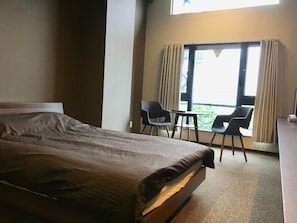 A hotel room with a bed, a small table, two chairs, and a window with curtains.