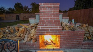 A brick fireplace with a fire burning inside, surrounded by wood logs. - Adorable House with fireplace in backyard (Santa Clarita)