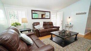 A living room with a brown leather sofa, a matching armchair, a coffee table with decorative items, a mirror, and a light fixture on the wall. - Adorable House with fireplace in backyard (Santa Clarita)