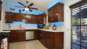 A kitchen with dark wooden cabinets, a ceiling fan, a built-in microwave, and a window with blinds. - Adorable House with fireplace in backyard (Santa Clarita)