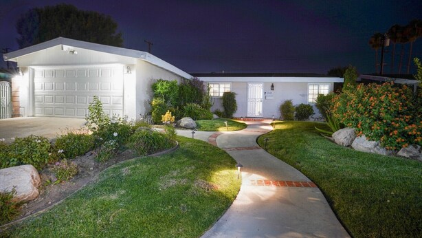 A two-story house with a garage, a driveway, and a well-maintained garden with various plants and flowers. - Adorable House with fireplace in backyard (Santa Clarita)