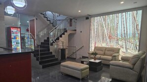 Uma sala de estar moderna com escada, sofá, mesa de centro e uma grande janela com vista para uma floresta.