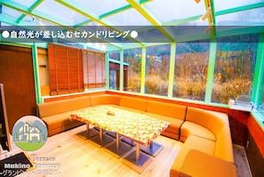 Une terrasse de style Makino, dotée d’une table et de bancs en bois, de grandes fenêtres et offrant une vue sur l’extérieur.