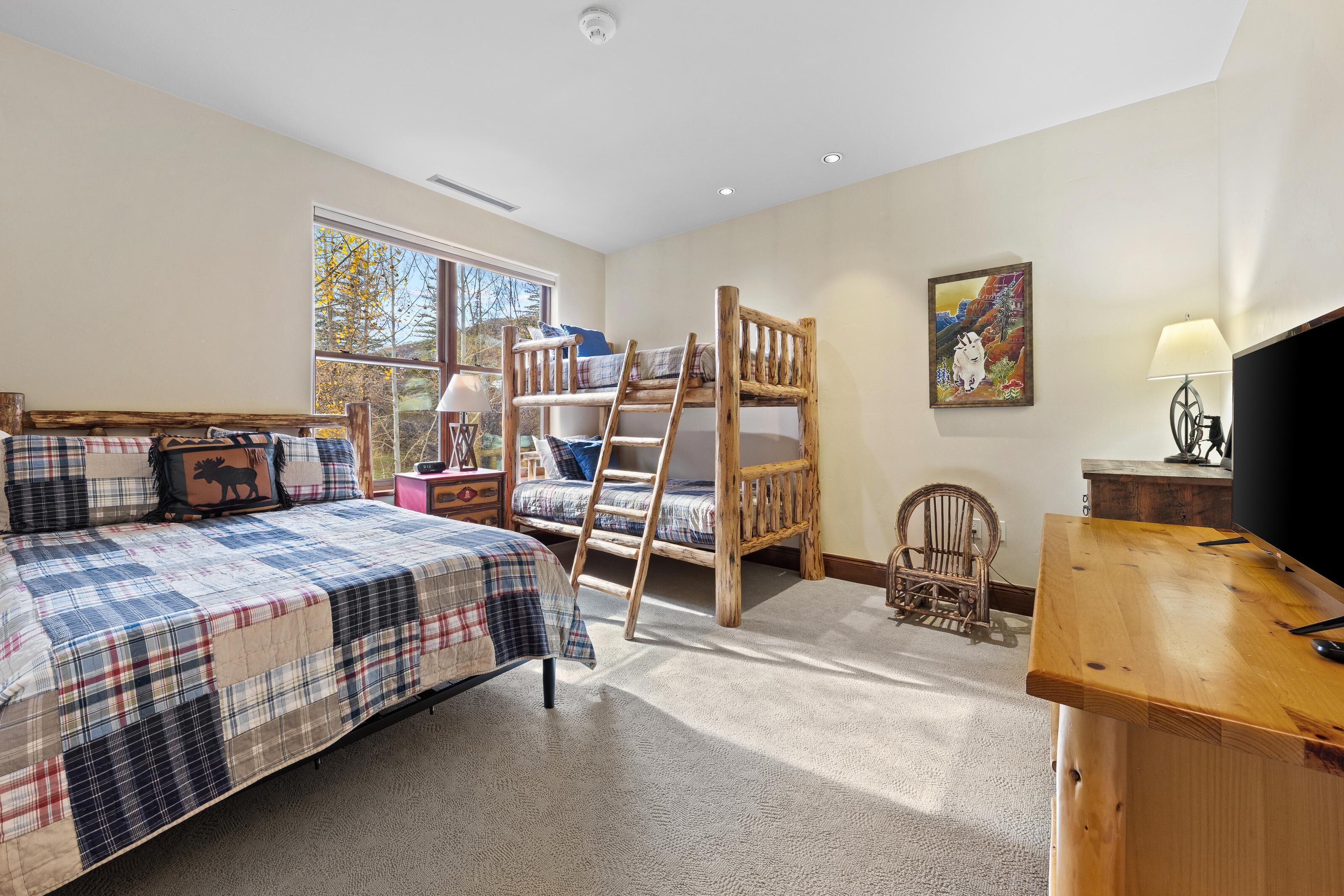 A bedroom with a bed, a wooden ladder, a chair, a desk, and a window.