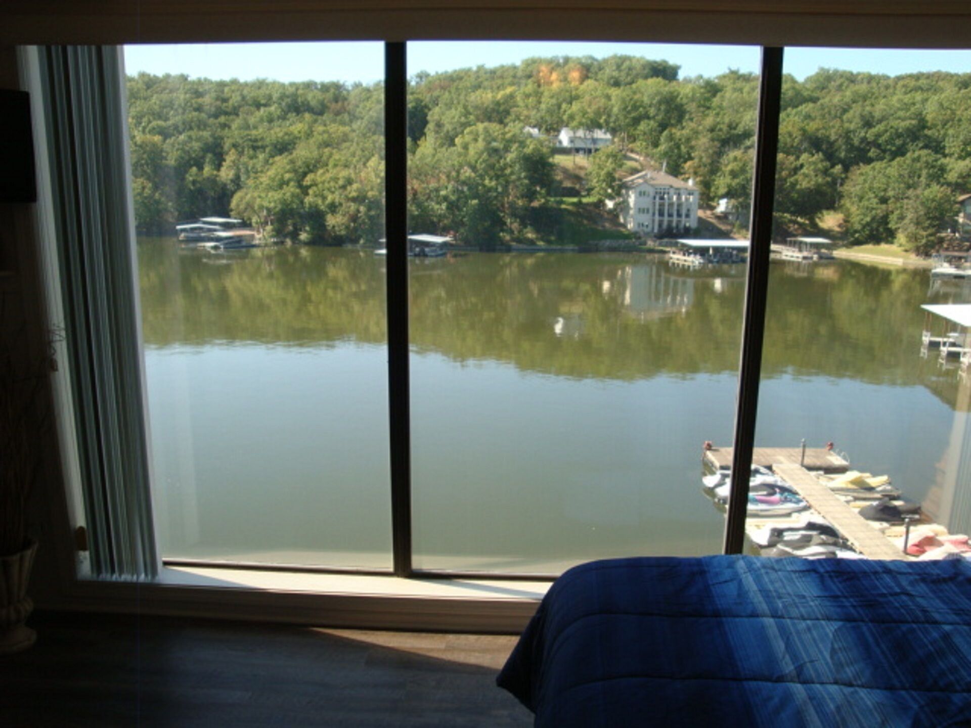 A room with a large window offering a view of a lake and dock with boats, surrounded by trees and houses.