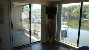 Ein Zimmer mit einer großen Schiebeglasdoor, die auf einen Balkon mit Seeblick und Booten führt.