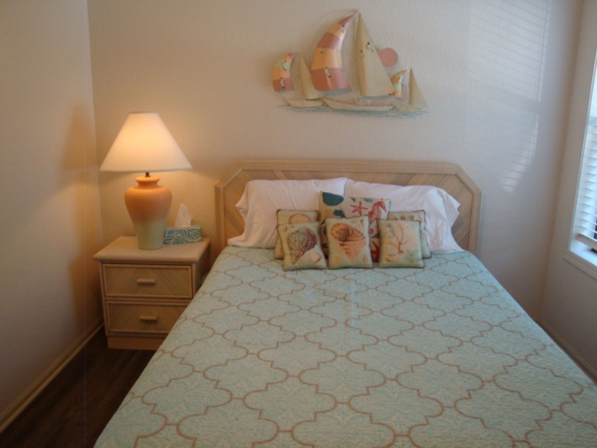 Een slaapkamer met een bed, nachtkastje, lamp en een decoratie van zeilboten aan de muur.