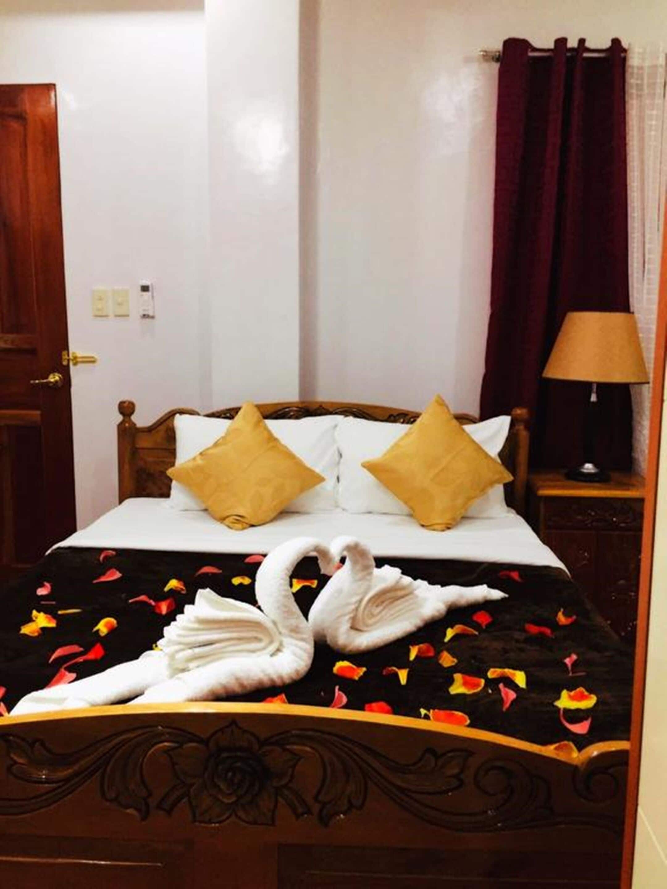A neatly made bed with two pillows, a wooden headboard, and a black bedspread with swan decorations.