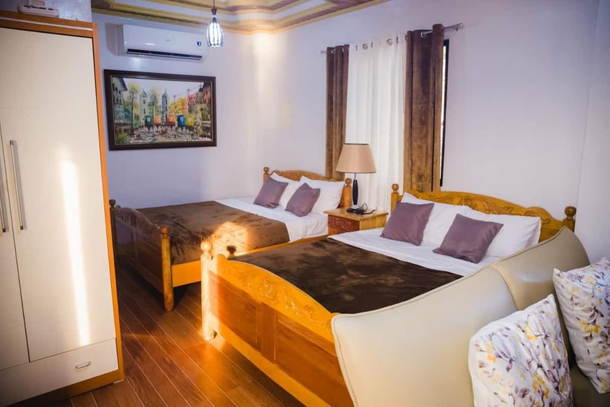 A hotel room with two beds, a wardrobe, a painting, and a window with curtains.