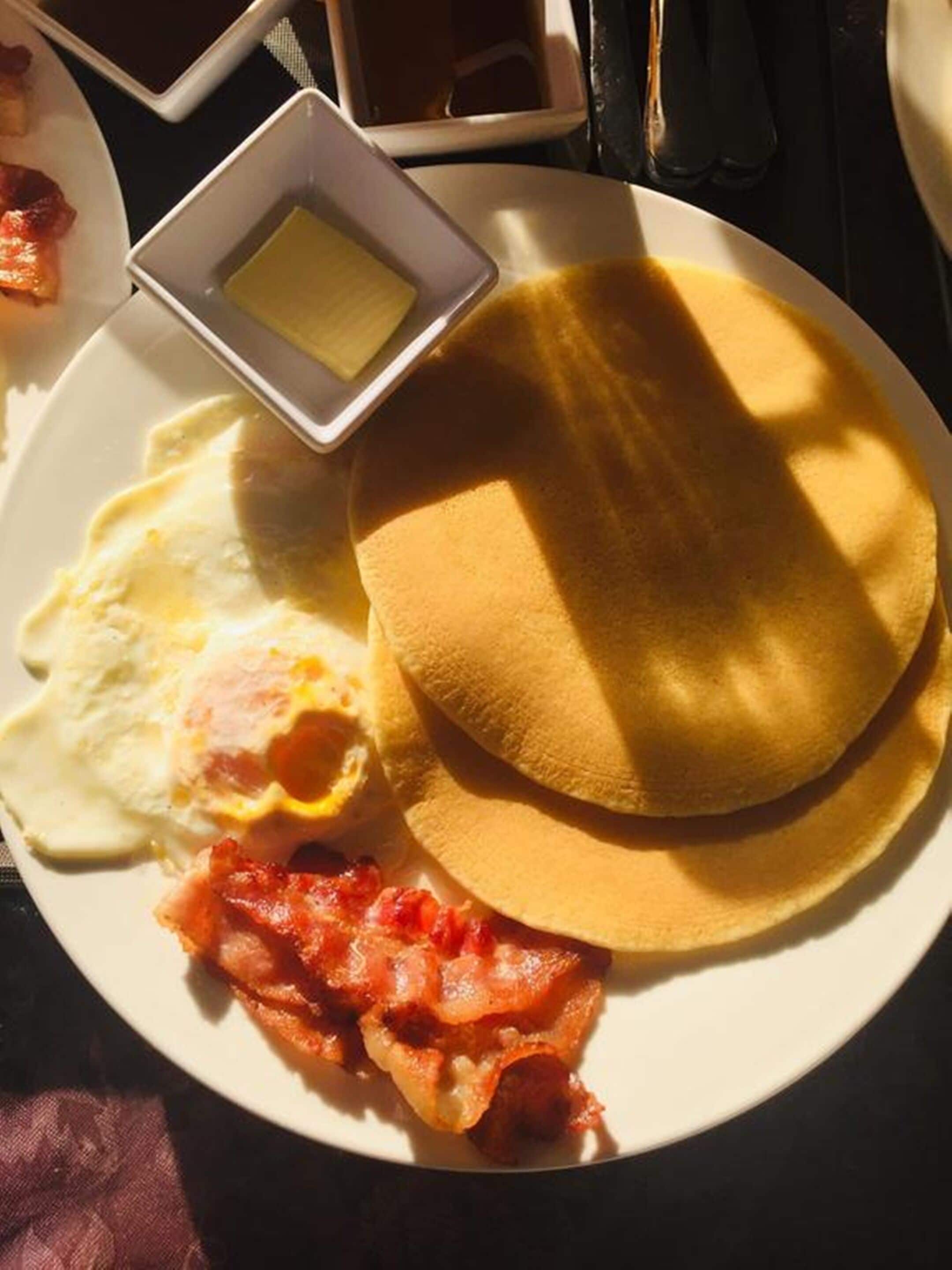 Une assiette de petit-déjeuner avec des œufs, du bacon, des toasts et du beurre.