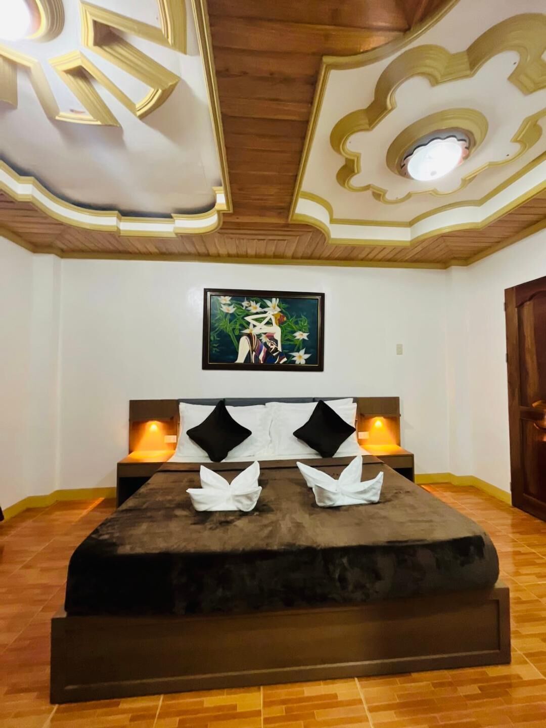 Un dormitorio con una cama grande, un cuadro en la pared y un techo de madera con molduras decorativas.