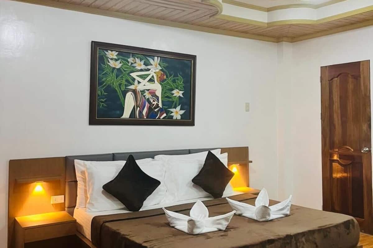 A bedroom with a bed, nightstands, a painting, and a wooden door.