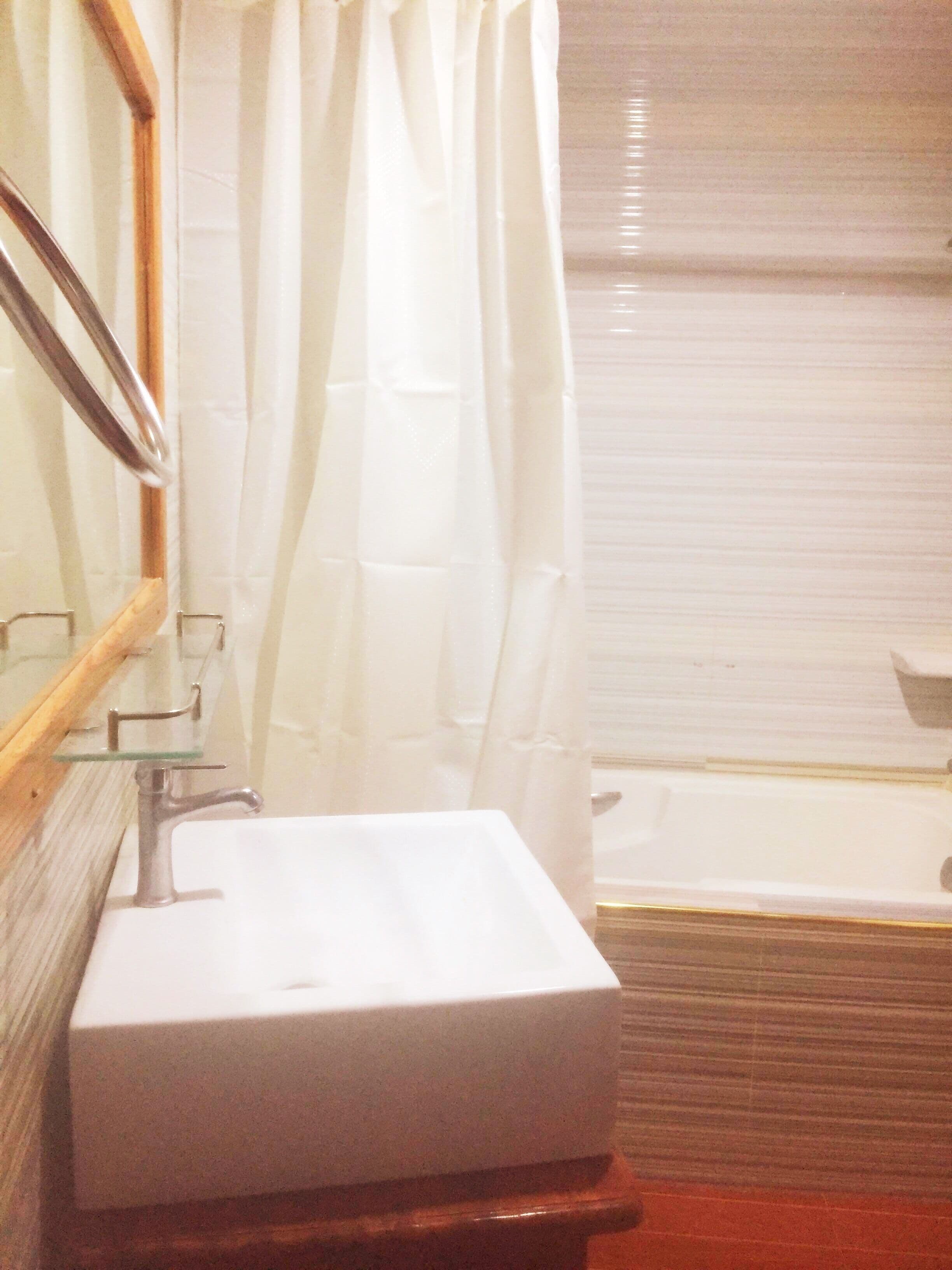 A bathroom with a white sink, a glass shelf, a wooden cabinet, a shower curtain, and a bathtub.