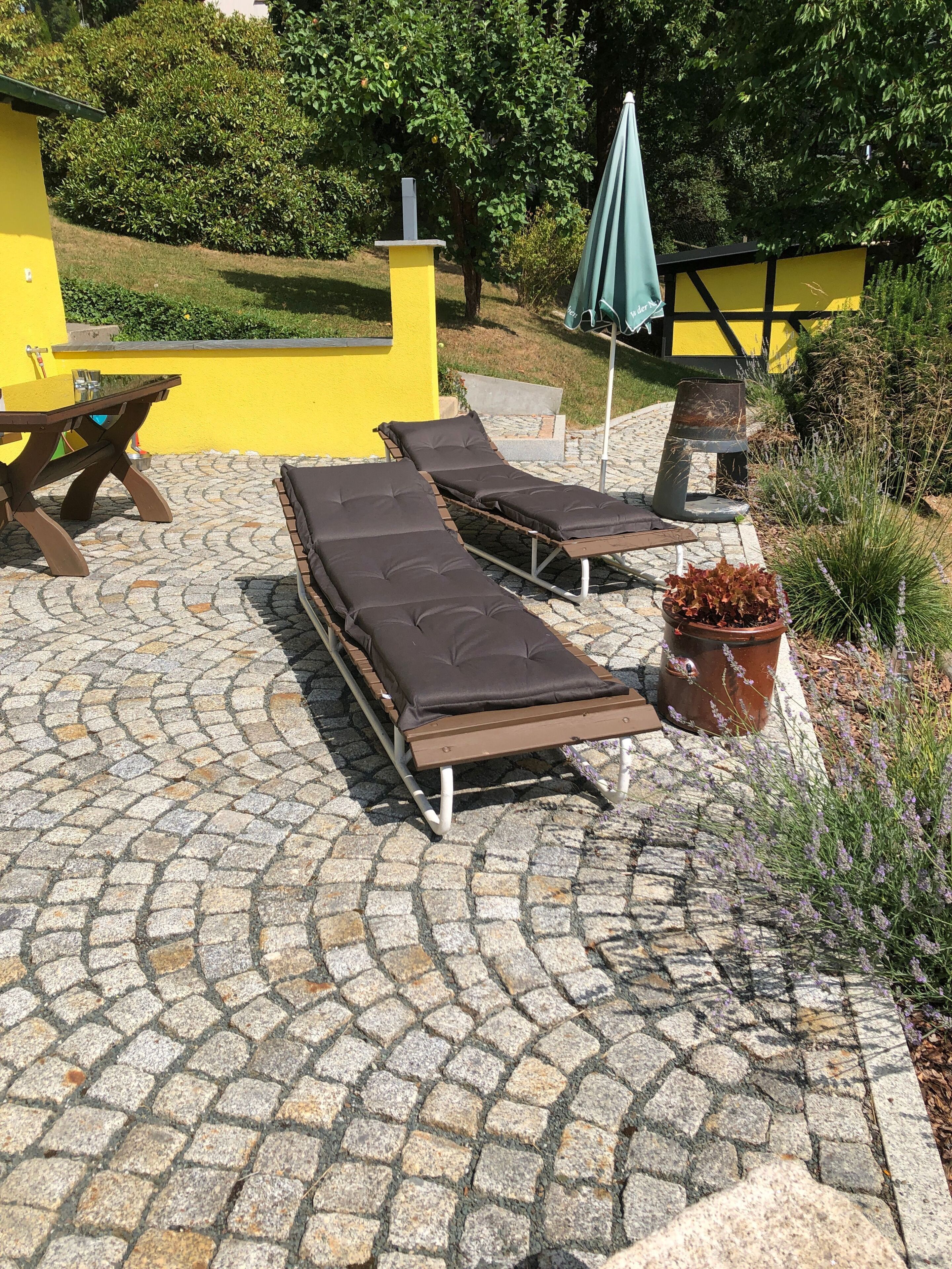 Un patio con sillas de descanso y una mesa, rodeado por un muro amarillo y follaje.