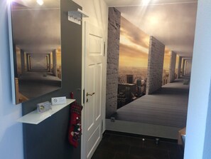 Un pasillo con un muro espejado, una puerta y un mural con un paisaje urbano.