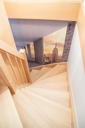 Una escalera de madera que conduce a un altillo con un mural de paisaje urbano en el techo.
