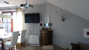 Un salon moderne comprenant un coin repas, un téléviseur fixé au mur, un radiateur et une tête de cerf décorative accrochée au mur.