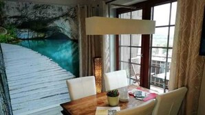 Un coin repas avec une table en bois, des chaises blanches, une vue sur un paysage rocheux par la fenêtre et une lampe.