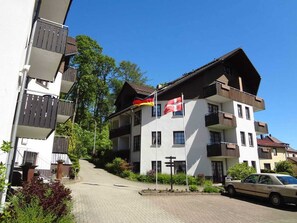 A multi-story building with balconies, a flag, and a car parked in front. - Hunting Lodge Harz (Bad Sachsa)
