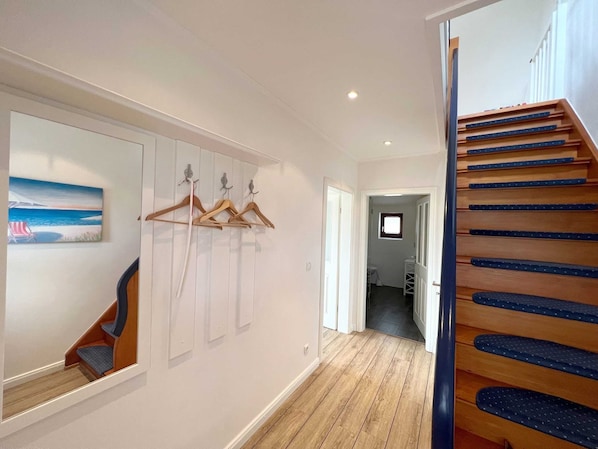 A hallway with wooden flooring, a staircase with blue steps, and a wall-mounted coat rack.