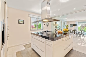 A modern kitchen with a central island, white cabinetry, and a large window.