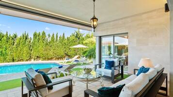 Un espacio exterior moderno con piscina, sillas de descanso, una mesa de vidrio y vistas a un área boscosa.