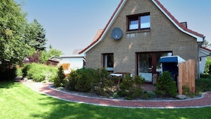 Ein zweistöckiges Haus mit Backsteinfassade, einer Satellitenschüssel und einem kleinen Garten mit gepflastertem Weg.