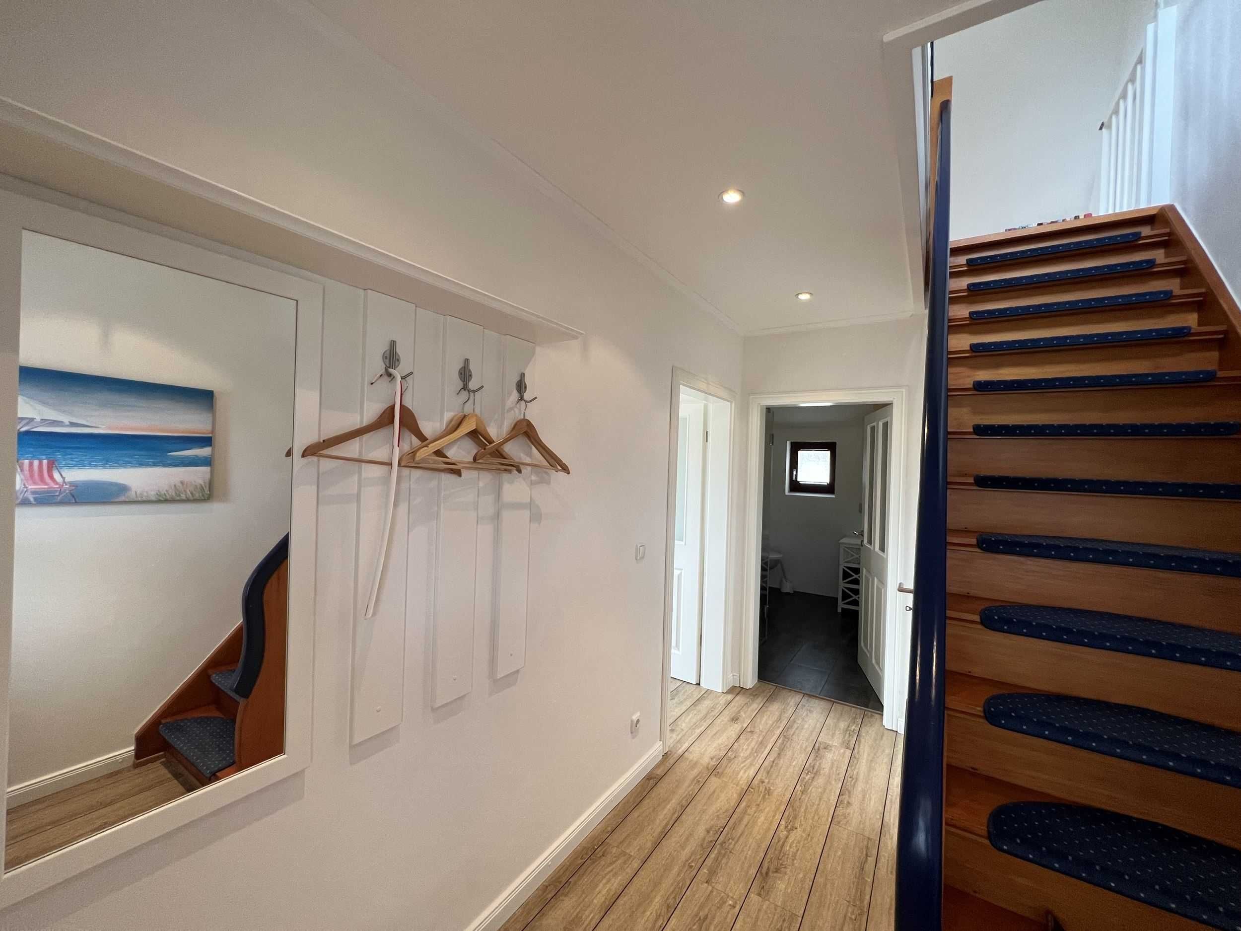 A hallway with wooden flooring, a staircase with blue steps, and a wall-mounted coat rack.