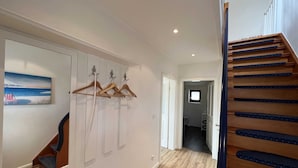 Ein Flur mit Holzboden, einer Treppe mit blauen Stufen und einem an der Wand befestigten Garderobenhaken.