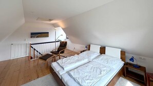 Ein Schlafzimmer mit Bett, Sessel, Schreibtisch und einer Treppe.