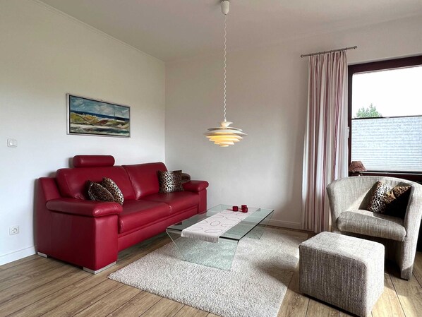 Un salon moderne avec un canapé rouge, un fauteuil gris, une table basse en verre et un luminaire suspendu.