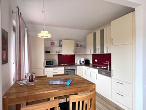 Une cuisine moderne avec des meubles blancs, une table à manger en bois et un pare-feu rouge.