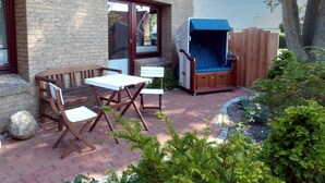 Eine Terrasse mit Backsteinmauer, Holzmöbeln und einer überdachten Sitzgelegenheit.
