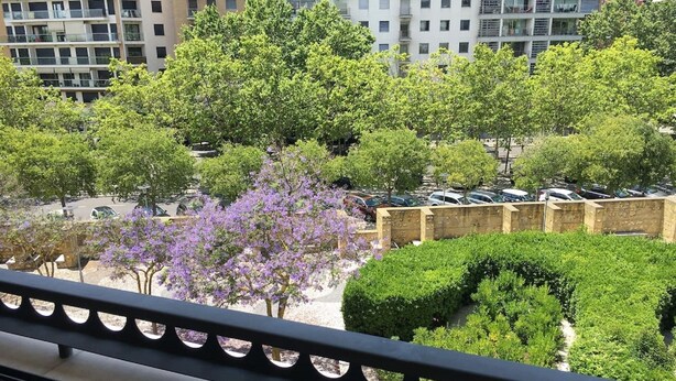 Une vue depuis un balcon donnant sur un parking bordé d’arbres, avec un bâtiment en arrière-plan.