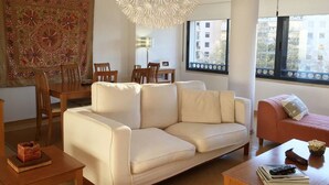 Un salon moderne avec un canapé blanc, un fauteuil rose, une table basse en bois et un coin repas comprenant une table et des chaises.