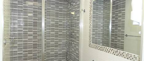 Un baño moderno con cabina de ducha de vidrio, un lavabo blanco y un espejo grande.