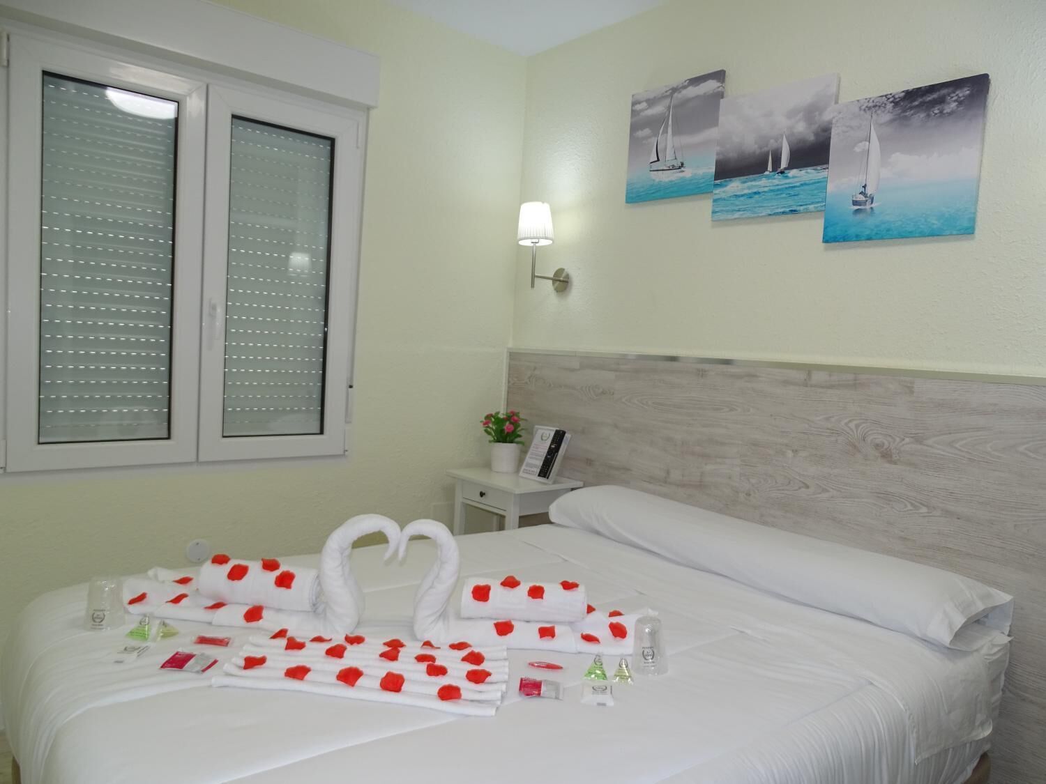 Una habitación de hotel con cama, mesita de noche, lámpara y ventana con persianas.