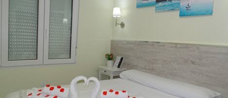 Una habitación de hotel con cama, mesita de noche, lámpara y ventana con persianas.