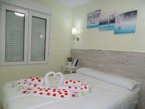 A hotel room with a bed, a nightstand, a lamp, and a window with blinds.